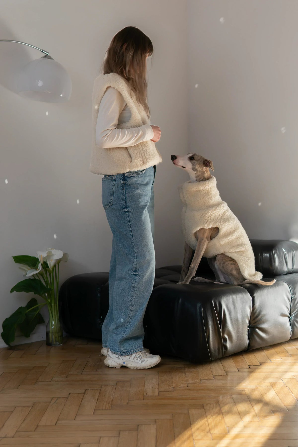 Sitzender Hund in weisser Mellow-Wollweste neben einer stehenden Frau mit passender Weste.