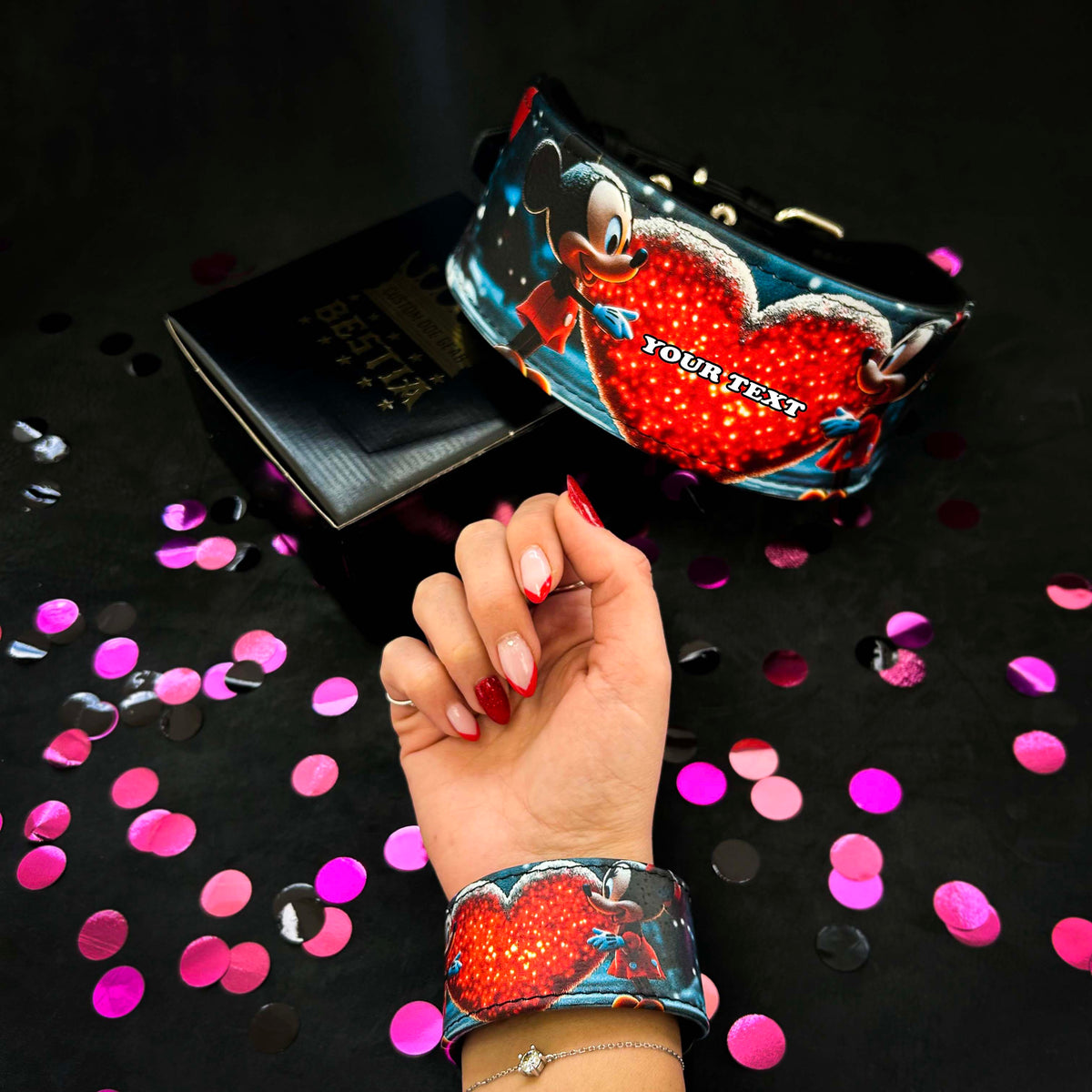 M&M-Armband am Handgelenk neben dem passenden Hundehalsband mit rotem Herz und dem Schriftzug «YOUR TEXT», umgeben von Konfetti