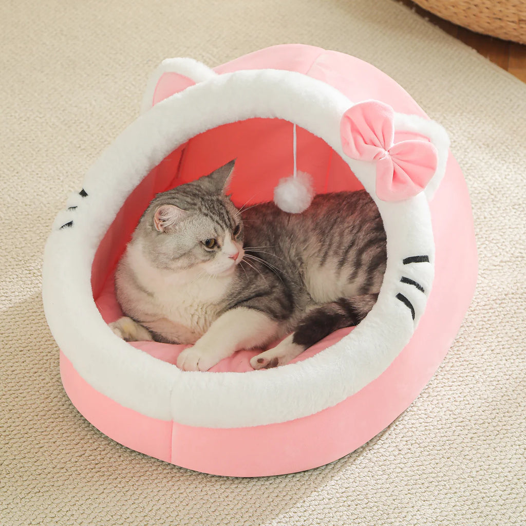 Getigerte Katze liegt in einer rosa Katzenhöhle mit weissem Plüschrand, rosa Schleife und hängendem Spielball