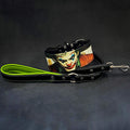 Schwarzes JK-Lederhalsband mit farbigem Joker-Motiv neben einer schwarzen Lederleine mit grüner Handschlaufenpolsterung und Metallkarabiner