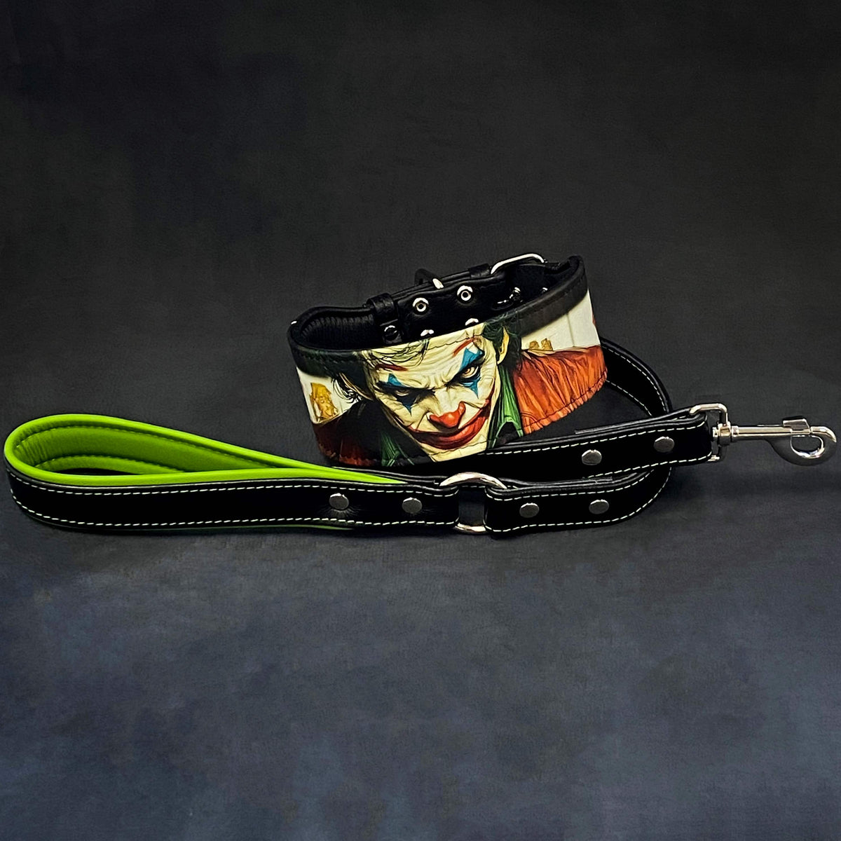 Schwarzes JK-Lederhalsband mit farbigem Joker-Motiv neben einer schwarzen Lederleine mit grüner Handschlaufenpolsterung und Metallkarabiner