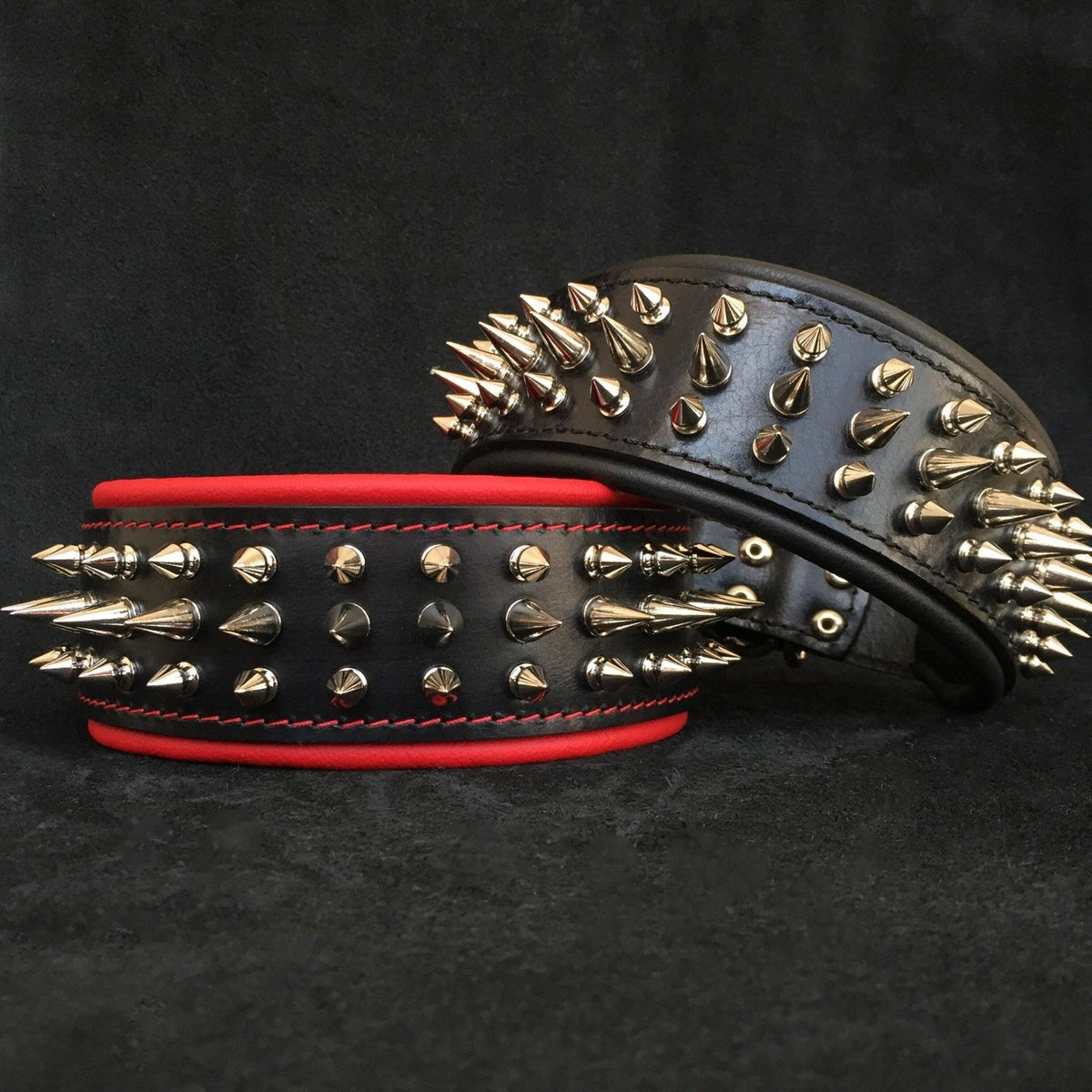 Zwei schwarze Danger-Lederhalsbänder mit metallfarbenen Spikes, eines mit roter und eines mit schwarzer Polsterung
