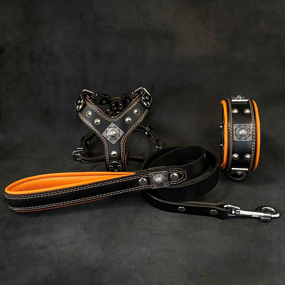 BESTIA EROS Hundeset aus schwarzem Leder mit Geschirr, Halsband und Leine, orangefarbener Polsterung und silberfarbenen Zierelementen.