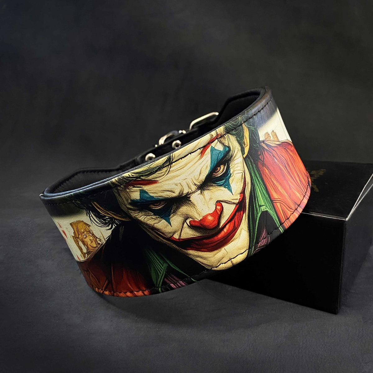 Nahaufnahme des schwarzen JK-Lederhalsbands mit farbigem Joker-Motiv und schwarzer Polsterung auf dunklem Hintergrund