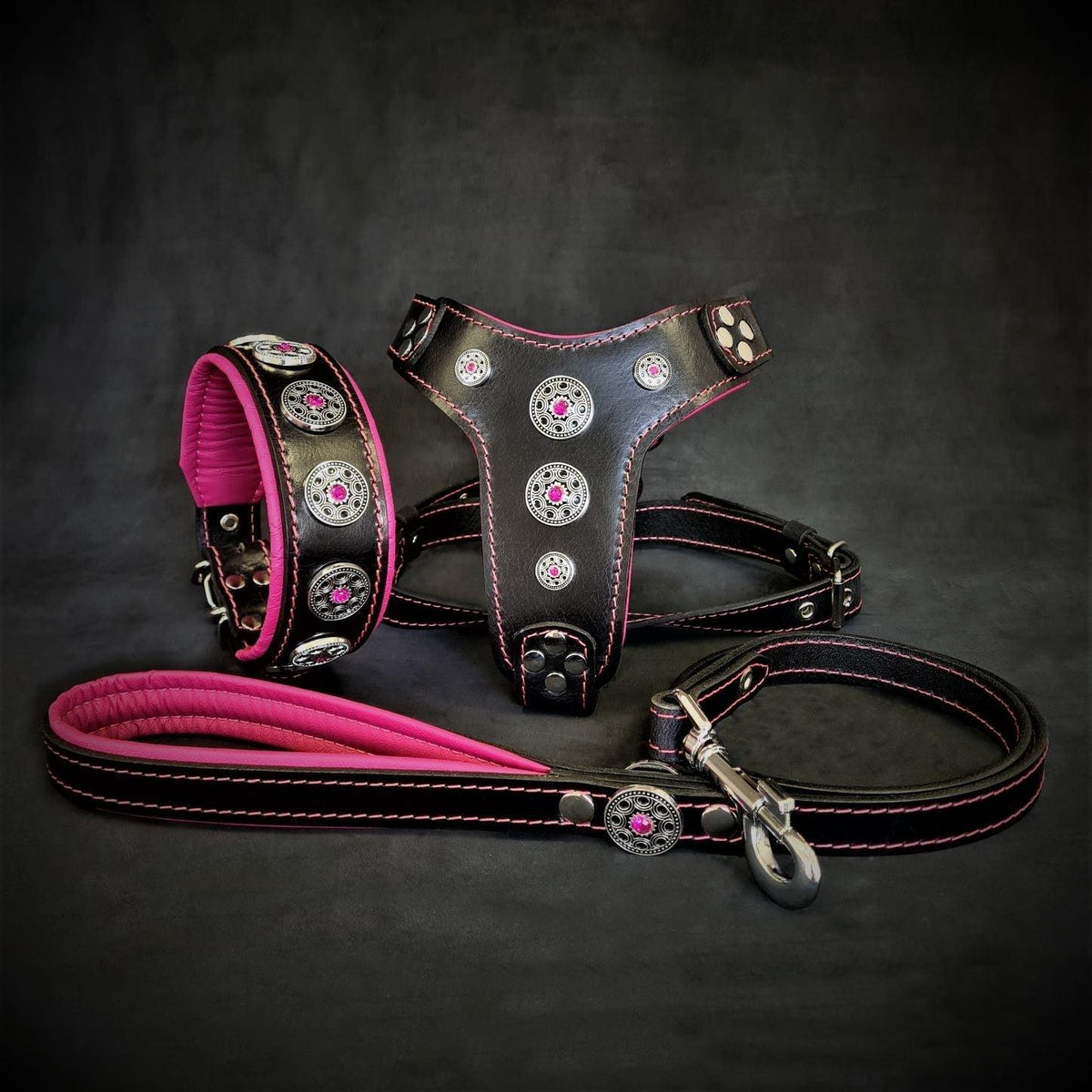 BESTIA Bijou Lederset mit schwarzem Halsband, Geschirr und Leine, pinkfarbener Polsterung und Nähten sowie silberfarbenen Zierelementen mit pinken Strasssteinen.