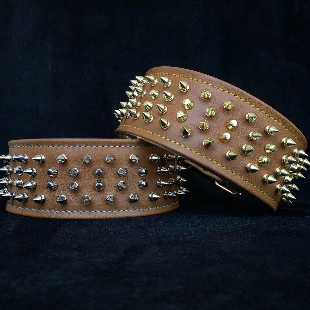 Zwei braune Crown-Lederhalsbänder mit silberfarbenen beziehungsweise goldfarbenen Spikes und Nieten auf dunklem Hintergrund